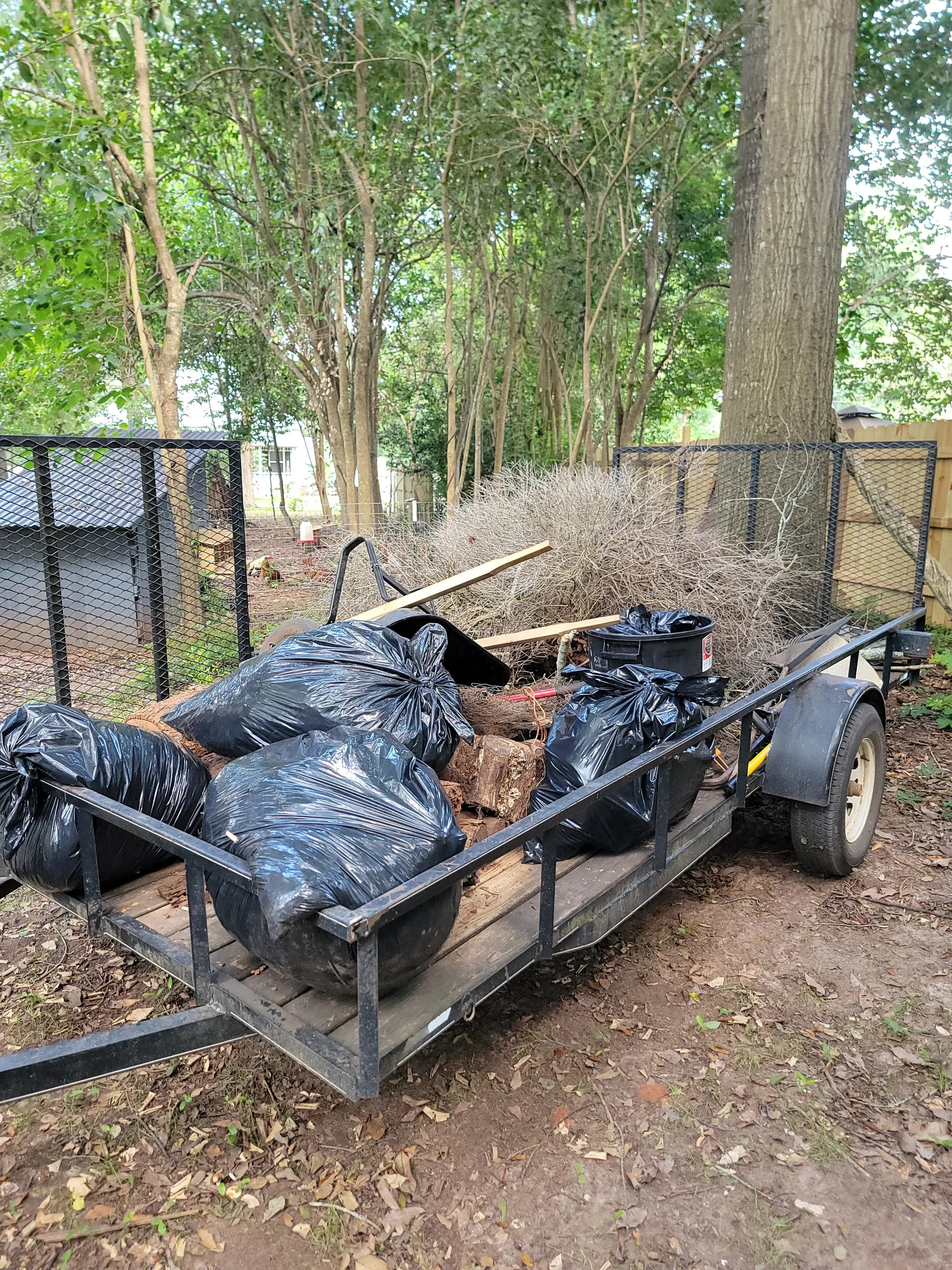Junk Be Gone utility trailer loaded with trash bags, brush, and other junk